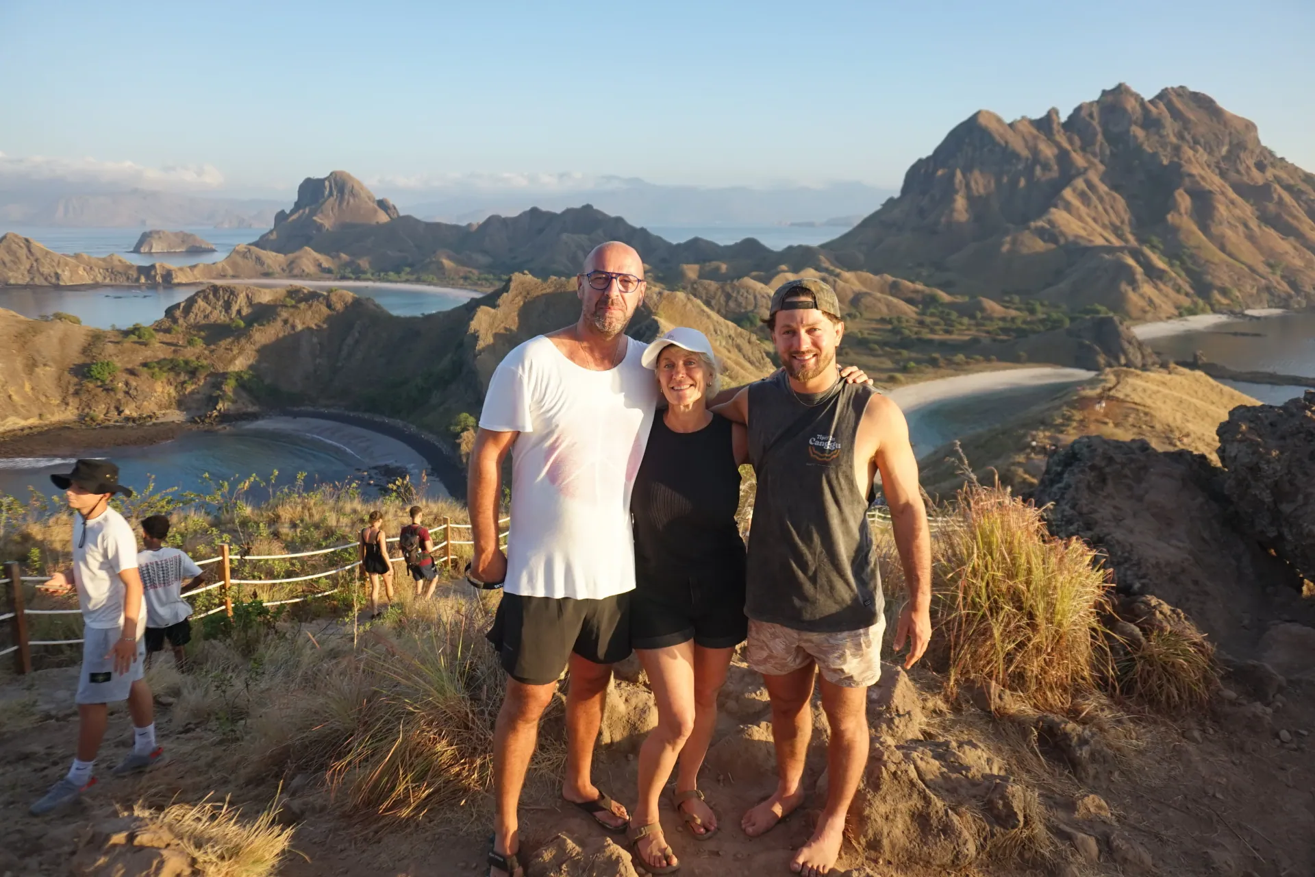 Three travellers standing on the Padar Island summit ridge with turquoise bays below