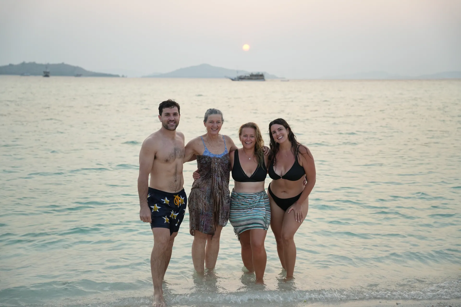 Travellers enjoying sunset by the shore with a Phinisi boat on the horizon near Labuan Bajo